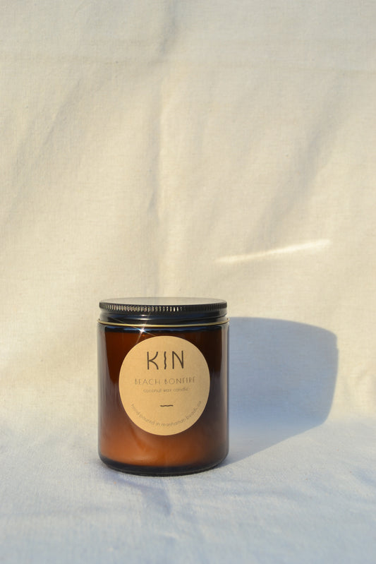 Beach Bonfire Candle by Kin candle Co. Carefree and nostalgic. Light this candle and instantly transport to blissful summer nights around the bonfire with scent notes of teakwood, smoke, and coconut.